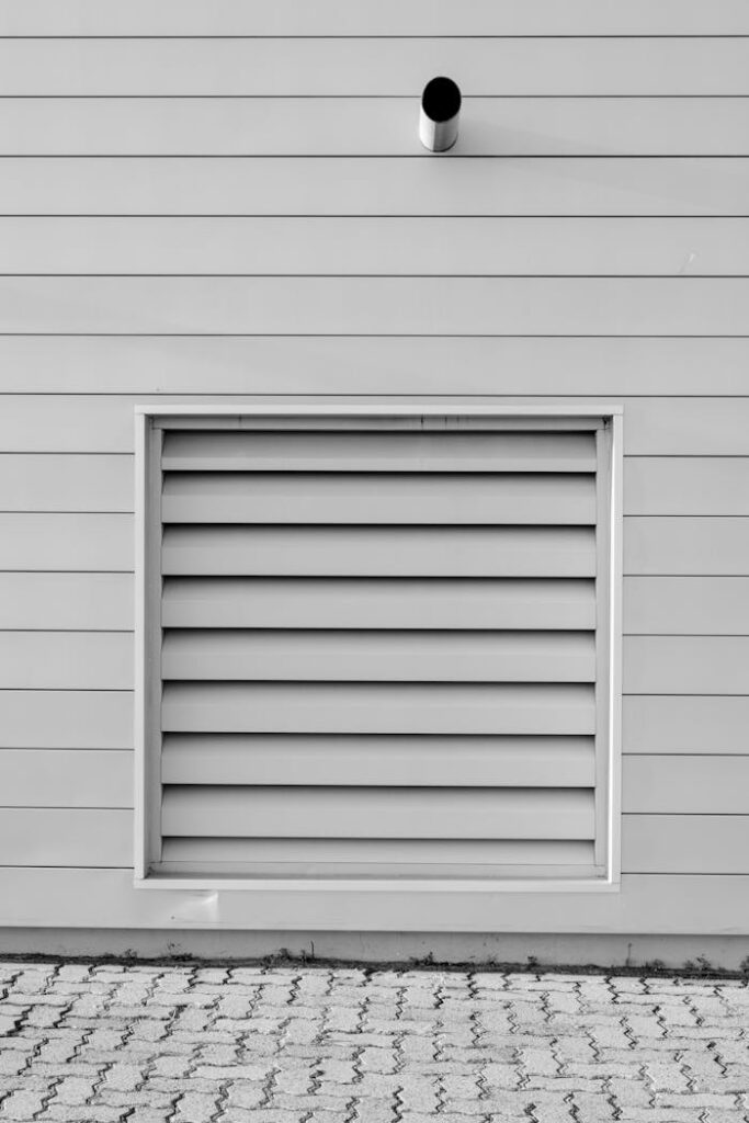 pexels photo 1567599 Black and white minimalist photo of an exterior wall with a vent and piping, capturing modern architecture.