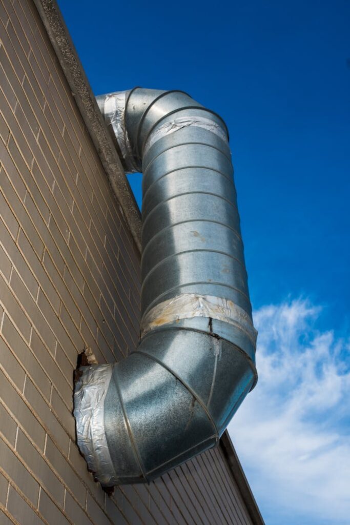 pexels photo 29086539 A large industrial air duct attached to a brick wall under a bright blue sky.