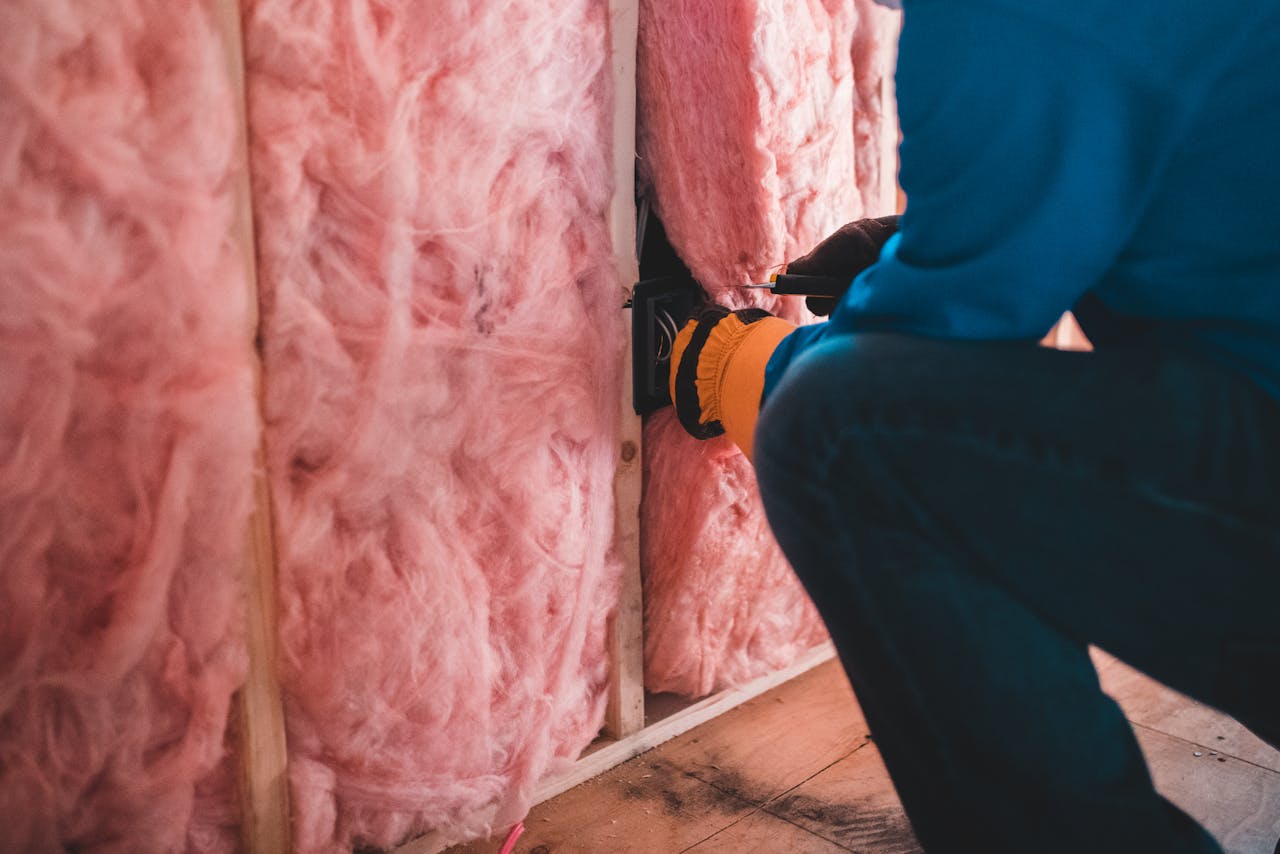 brand-01 Crop unrecognizable worker in gloves sitting on haunches and insulating with pink stone wool